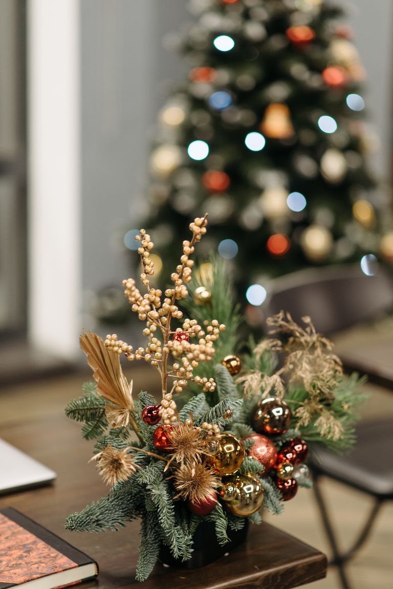 A beautifully decorated Christmas table centerpiece with a blurred tree in the background.