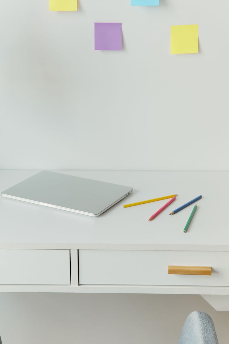 A minimalist home office desk with a laptop and colored pencils on a white surface.