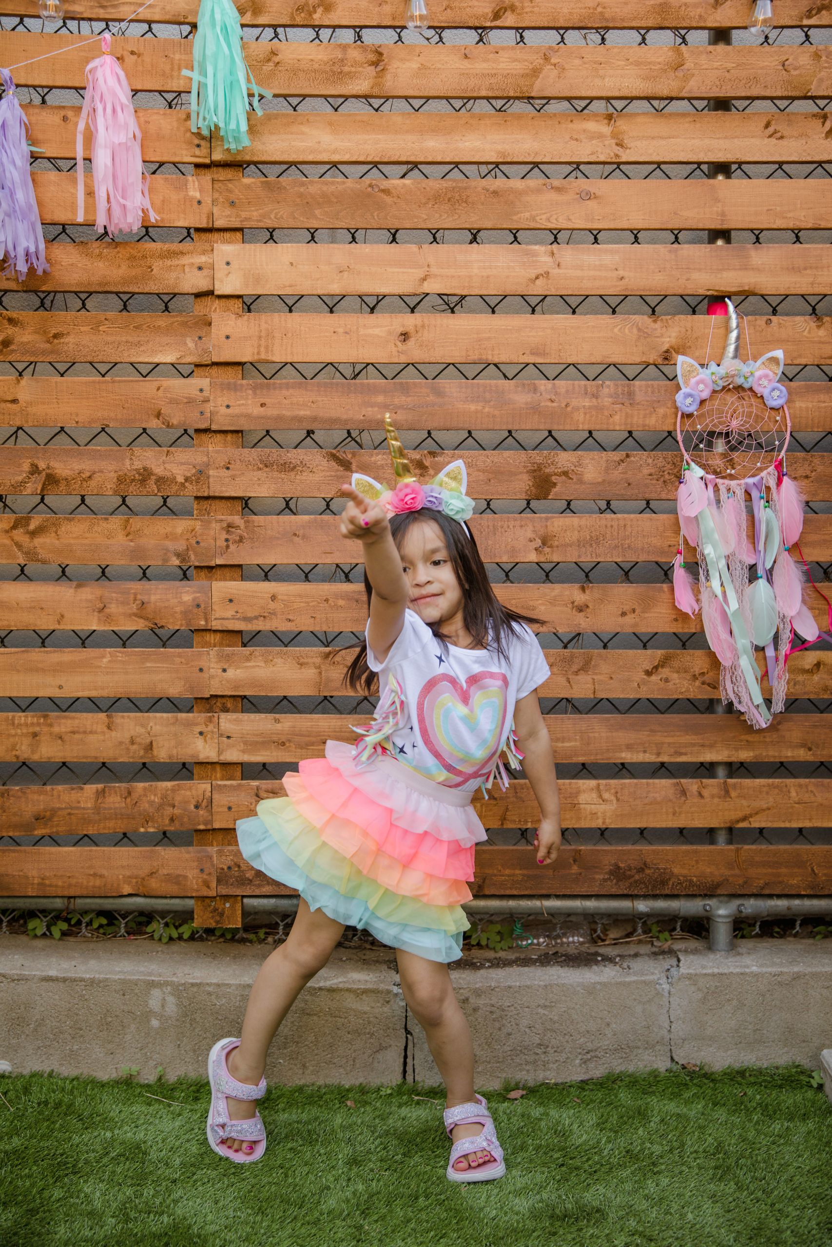 A young girl dressed in unicorn attire enjoying an outdoor birthday party with vibrant decorations.