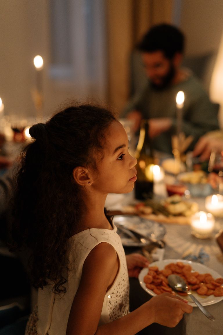 A young girl holds a plate during a cozy holiday dinner indoors with family.