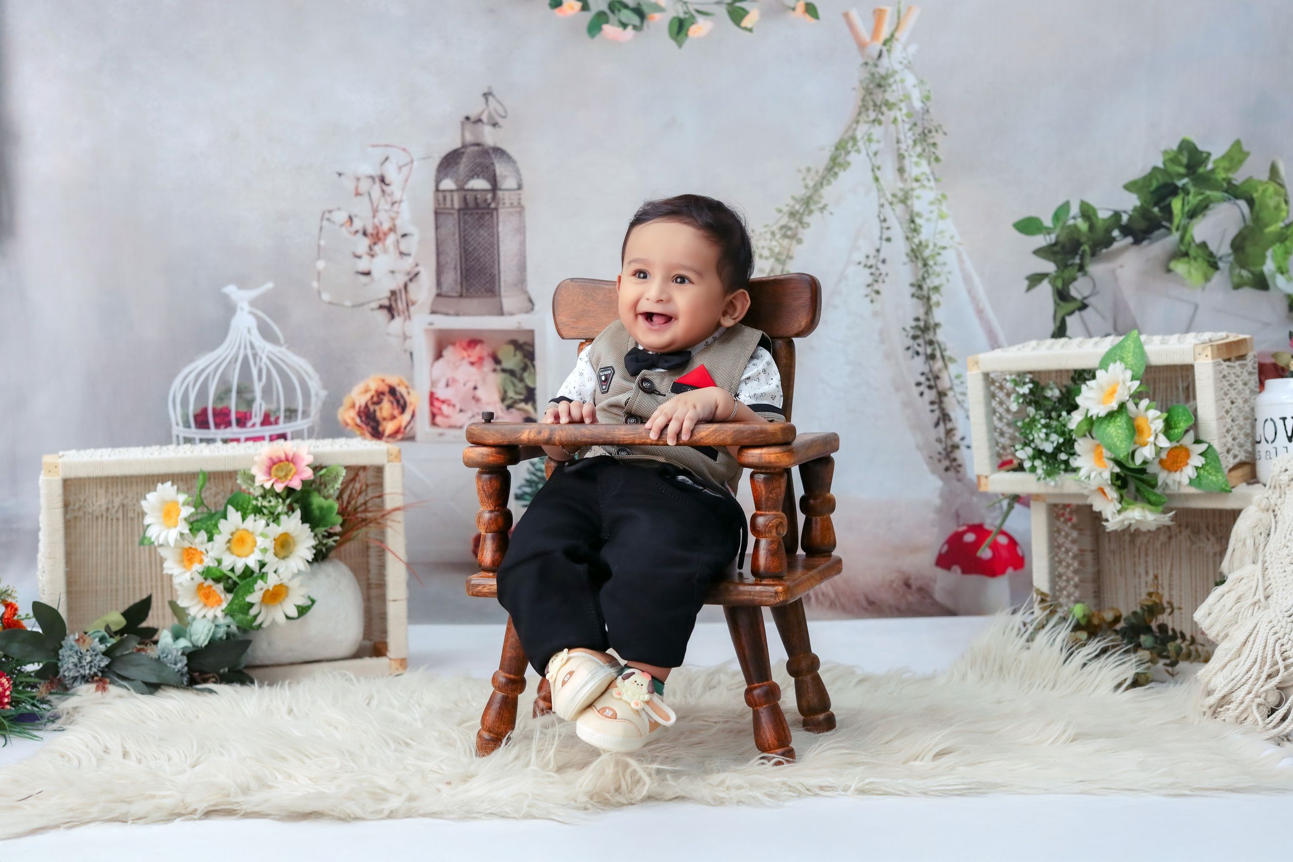 Adorable baby sitting in a wooden chair surrounded by floral decor, smiling indoors.