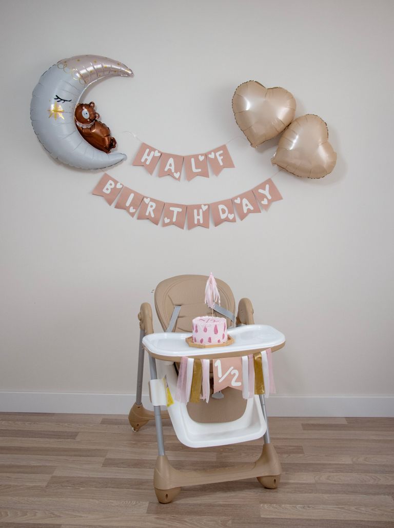 Adorable half birthday setup featuring a decorated high chair and balloons indoors.