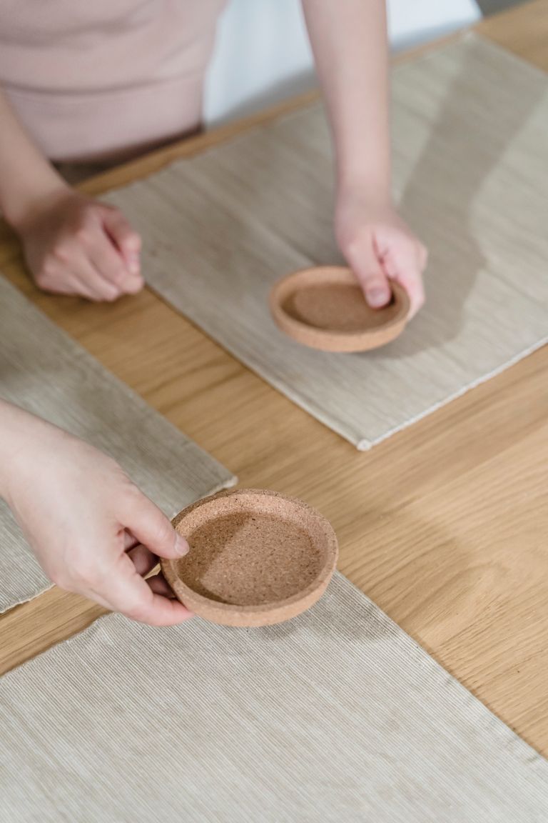 Close-up of people setting cork coasters on a table with beige placemats, creating a minimalist dining scene.