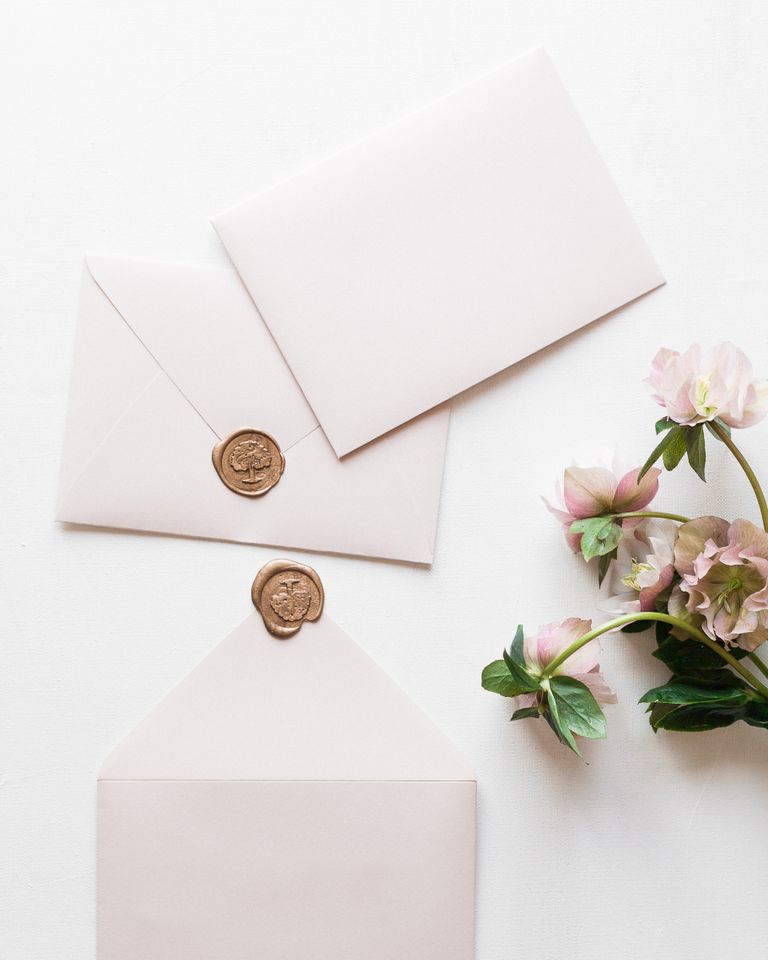 Elegant photo of white envelopes with wax seals and pink flowers, perfect for invitations.