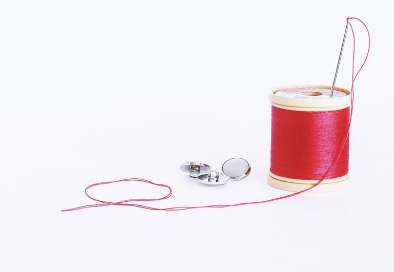 Red thread spool with a needle and buttons, ready for tangle-free hand sewing