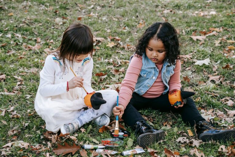 Little girls painting pumpkins together on the grass at my pumpkin painting station