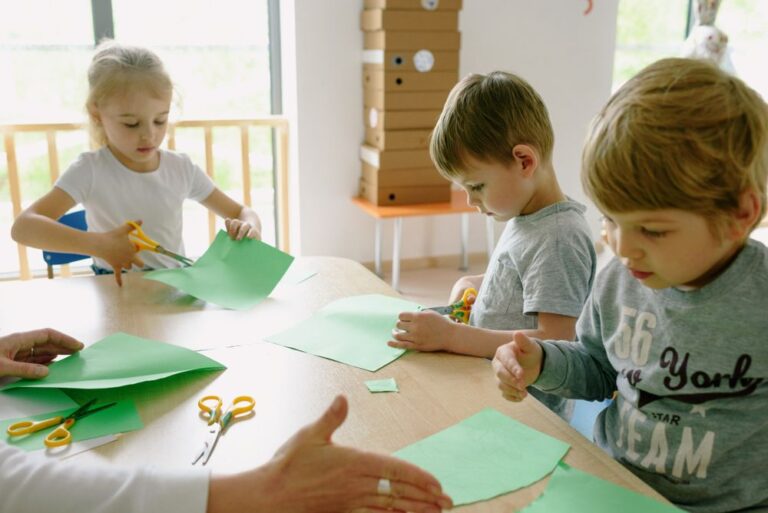 Students linking rainbow paper chains with scissors and colored paper strips in a bright classroom