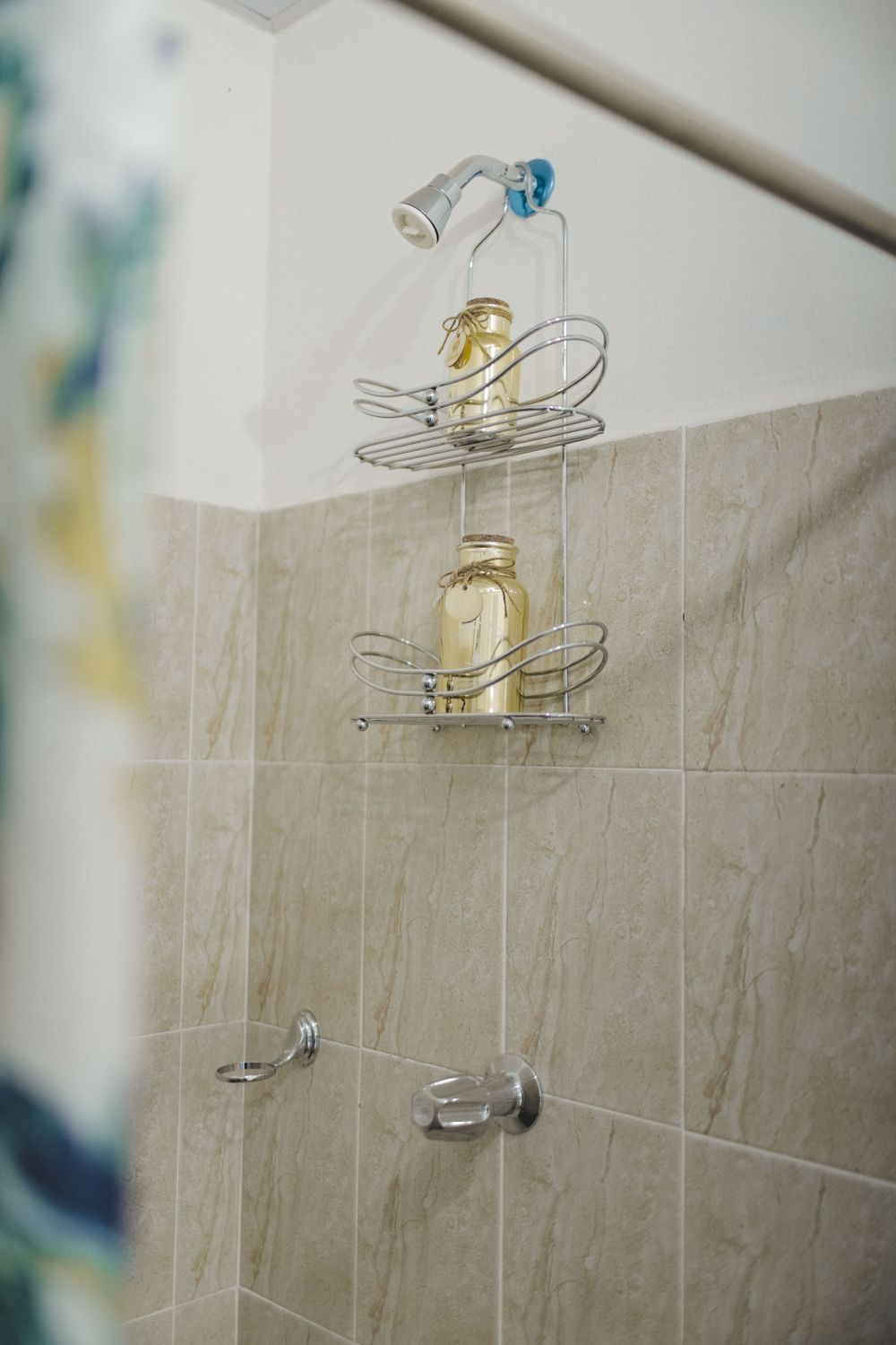 Vertical shot of a shower with a sleek wire shelf holding jars against tiled walls. Stock Photo.