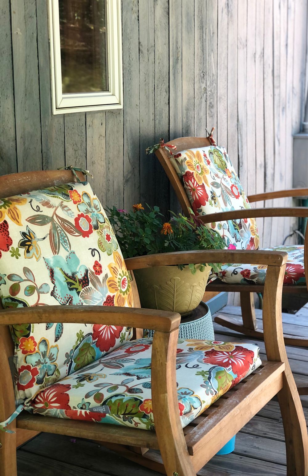 Two wooden armchairs with vibrant floral cushions on a cozy porch setting. Ideal for relaxing moments. Stock Photo.