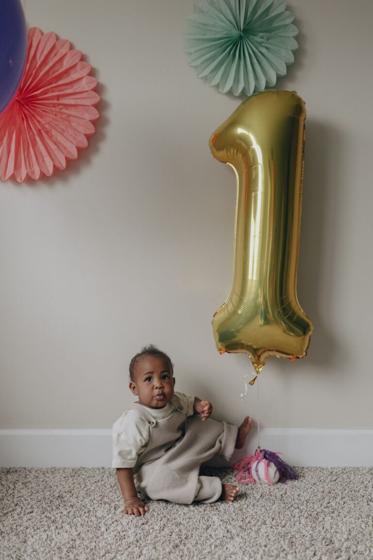 Cute baby celebrating first birthday with gold number one balloon indoors. Stock Photo.