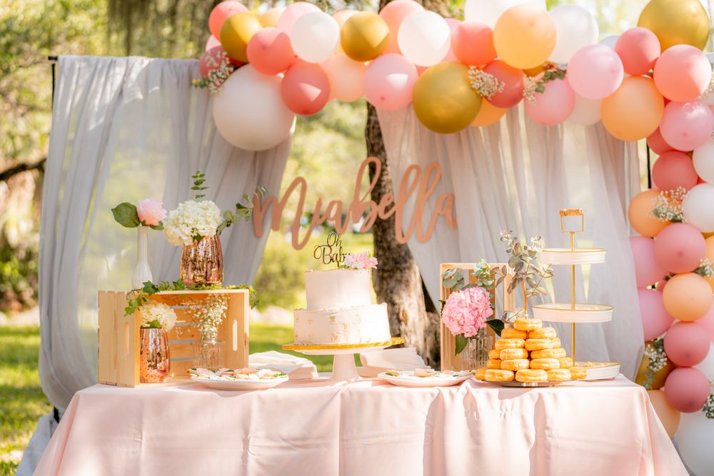 Delightful baby shower table with cake, balloons, and dessert display in an outdoor garden setting. Stock Photo.