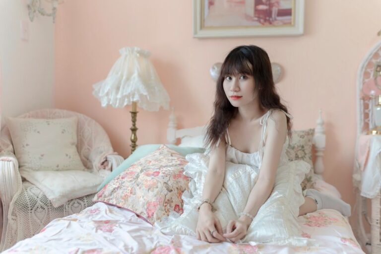 Young woman in a vintage-inspired bedroom with floral decor, exuding a cozy and peaceful vibe. Stock Photo.