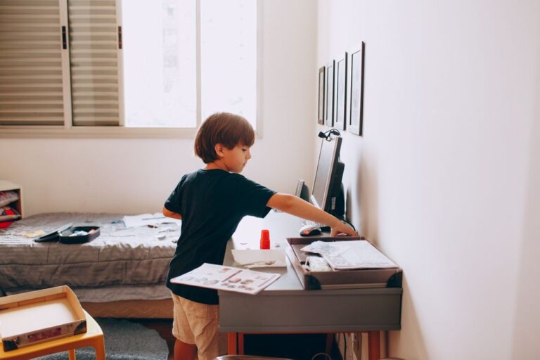 A young boy focuses on creative work at his desk in a cozy bedroom setting. Stock Photo.