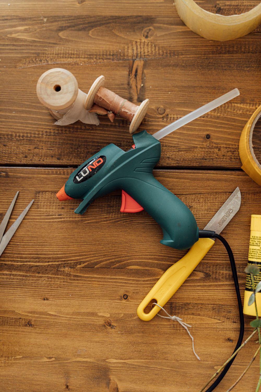 Hot glue gun and crafting tools laid out on a wooden table, ready to make a rope basket