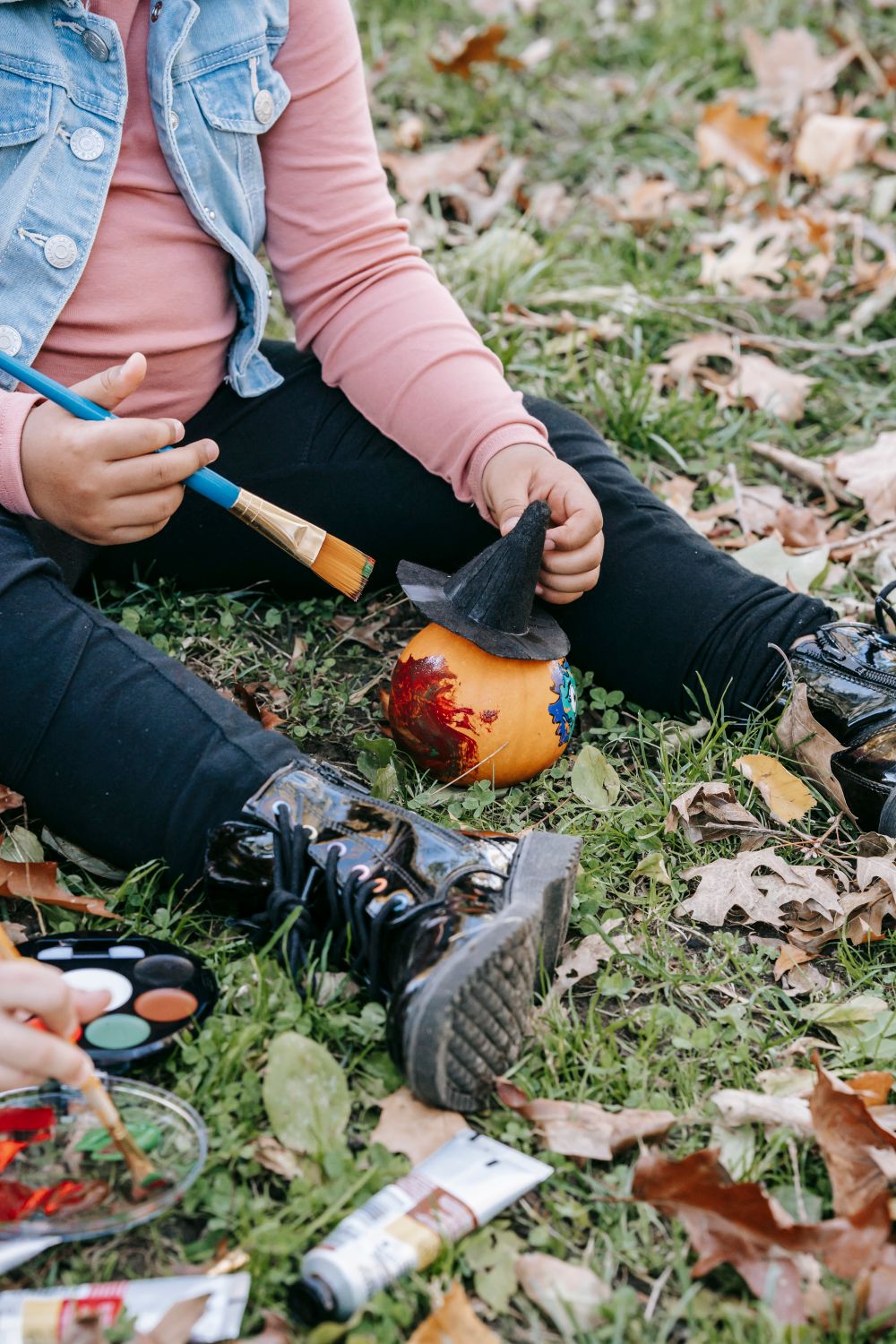Child painting a small pumpkin with watercolors for a fall art activity