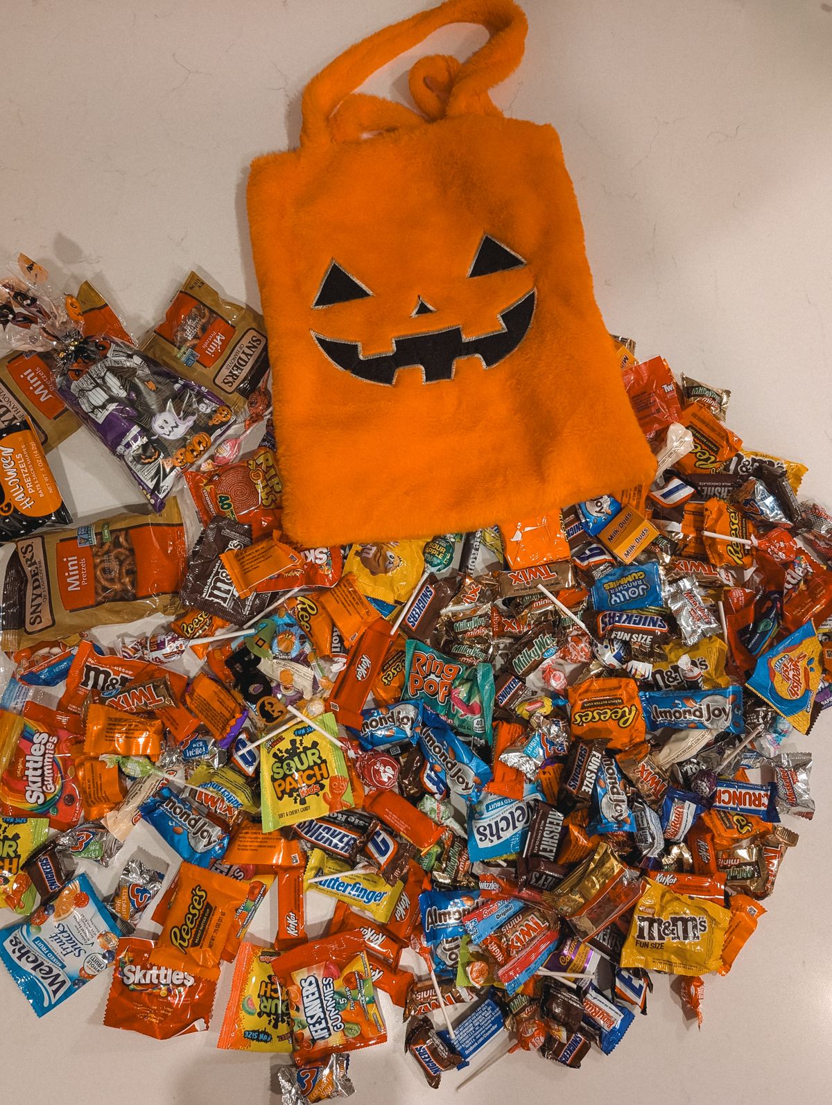 Overflowing pile of Halloween candies beside a pumpkin treat bag