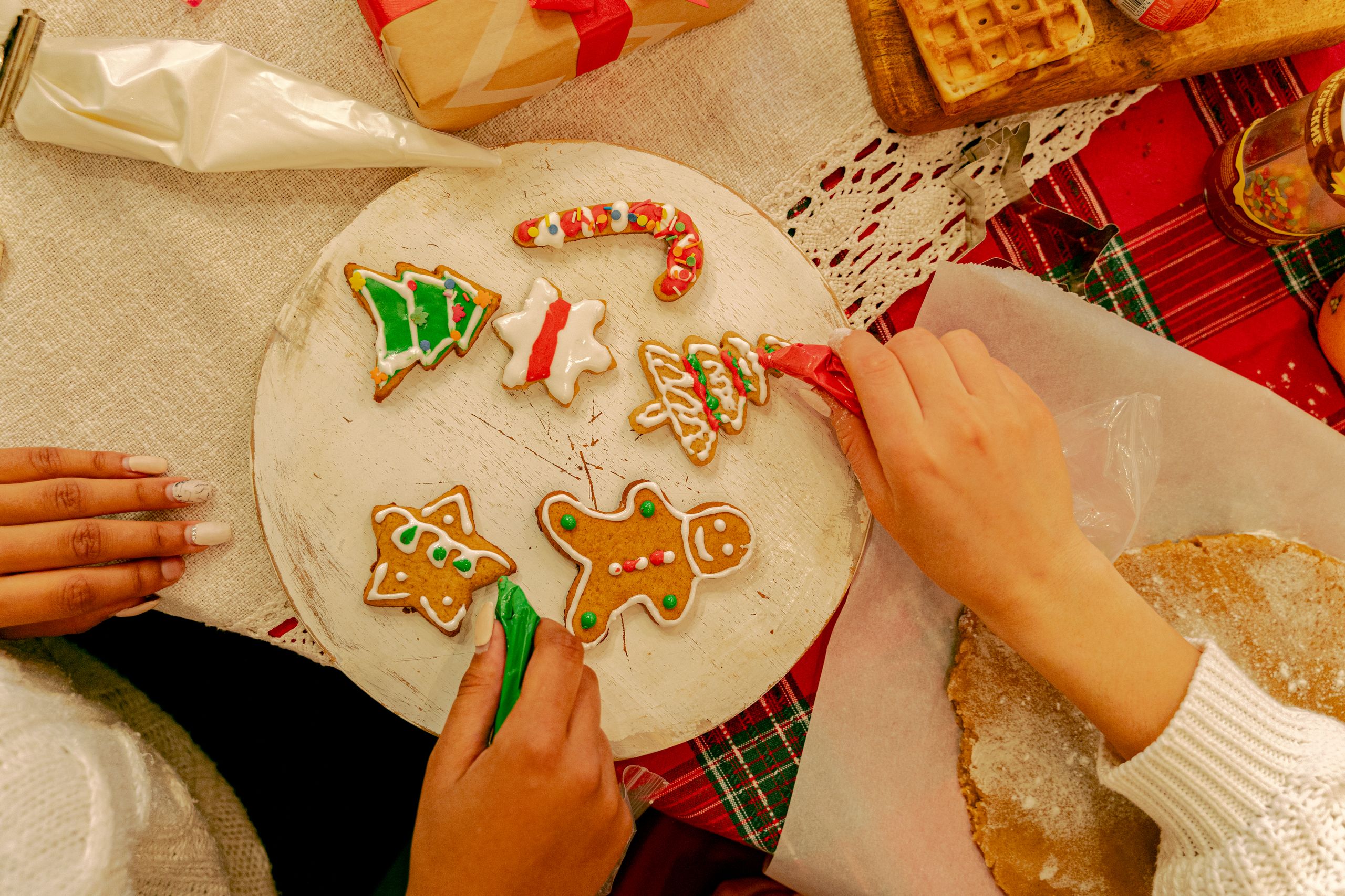 Hands decorating colorful gingerbread cookies for Christmas on a festive table.