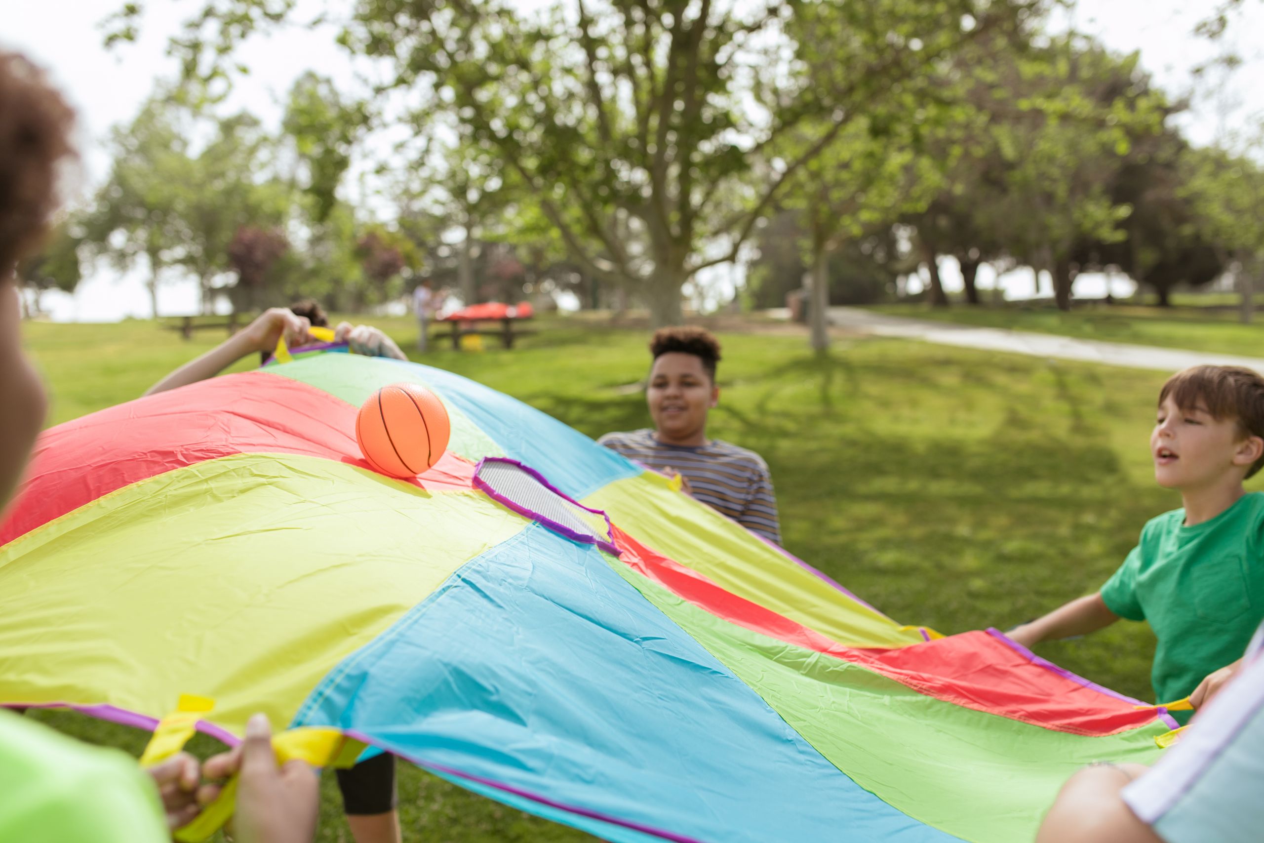Kids enjoying a fun outdoor game with a colorful parachute and ball in a park setting.