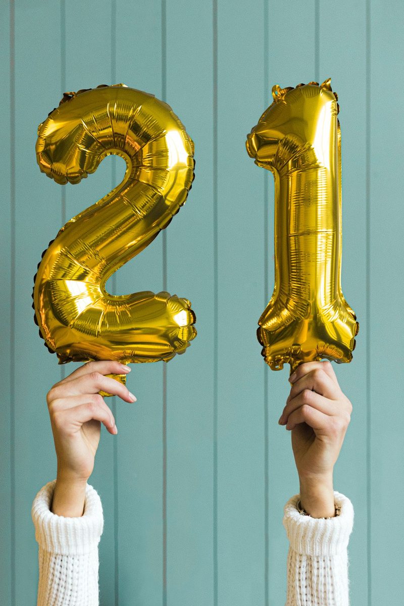 Milestone birthday decor ideas with gold number balloons held up at a celebration