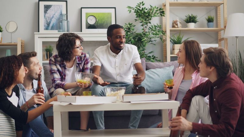 Surprise birthday party ideas with friends sitting around a table in a living room for a decoy dinner reveal
