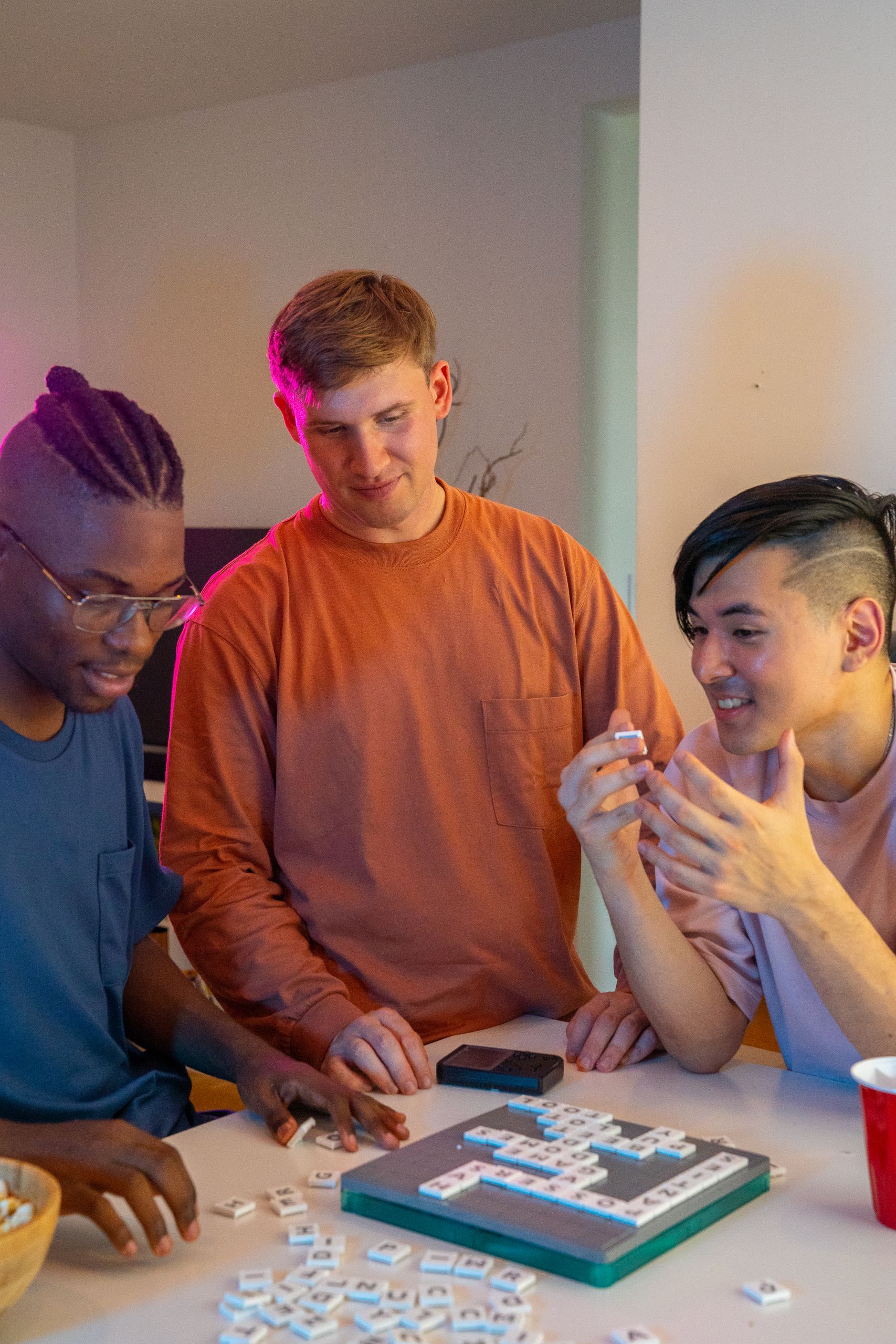 Three friends enjoying a Scrabble game at home with laughter and excitement.