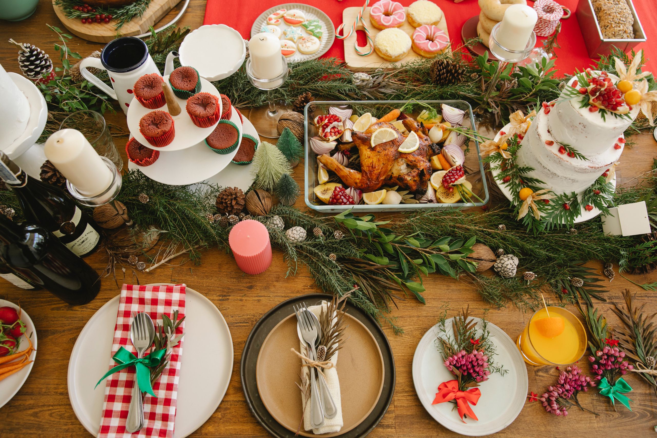 Top view of wooden table decorated with coniferous branches cutlery on plates and baked meat near cake with donuts during Christmas celebration