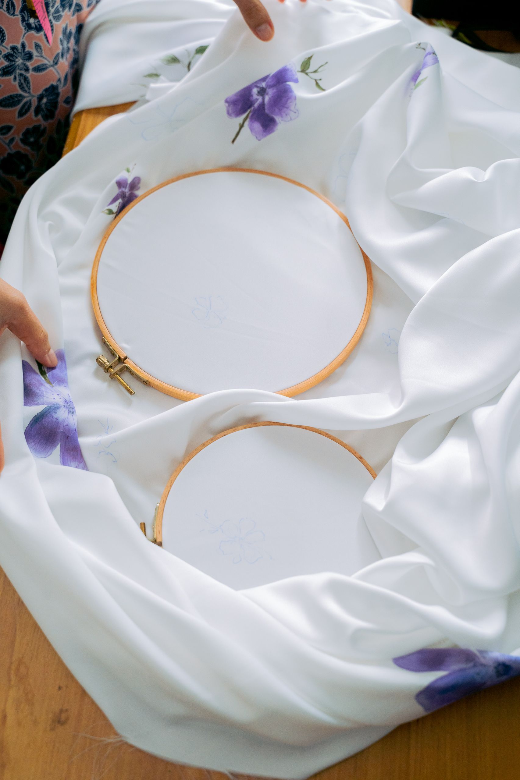 Two embroidery hoops placed on white fabric featuring purple floral designs, perfect for crafting inspiration.
