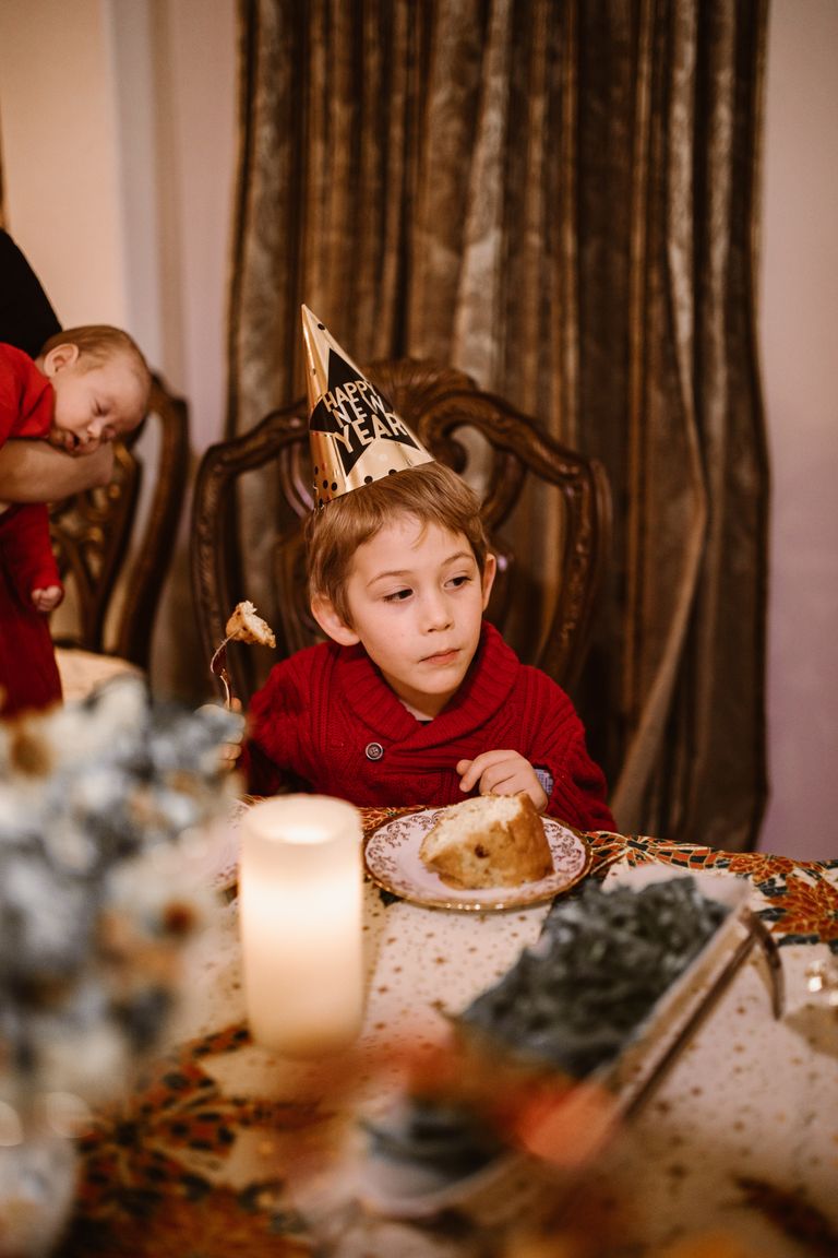 Young boy in party hat enjoying dessert at a New Year's celebration indoors.