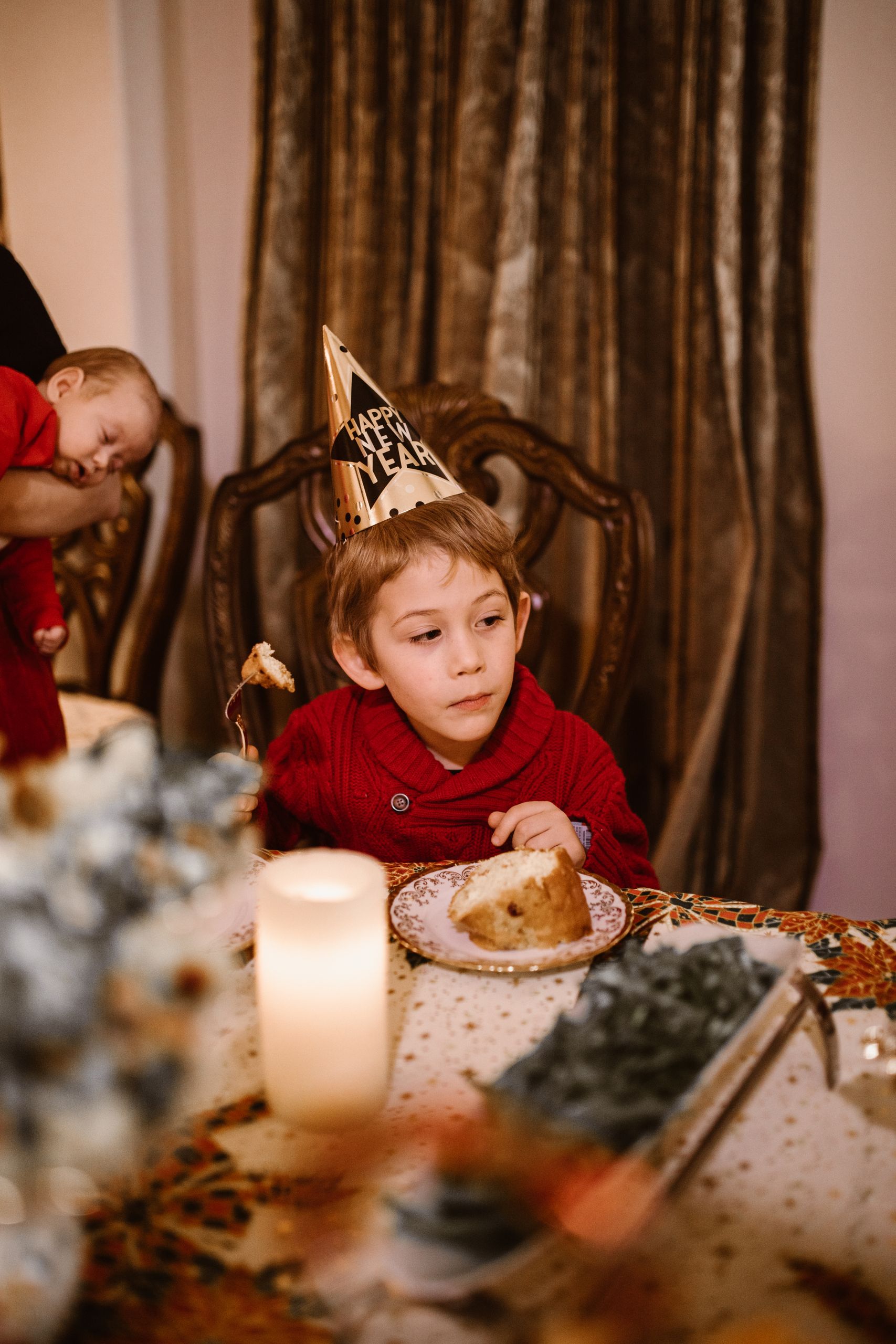 Young boy in party hat enjoying dessert at a New Year's celebration indoors.